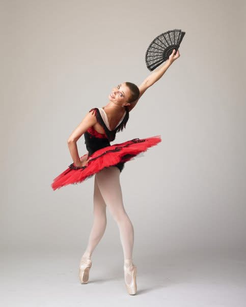 Principal Dancer Elena Shokhina as Kitri, performing on pointe in a red and black tutu with a lace fan